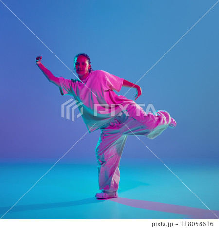 Stylish and artistic young girl moving with energy and passion, dancing hip-hop against gradient blue background in neon light Stylish and artistic young girl moving with energy and passion, dancing hip-hop against gradient blue background in neon light 118058616