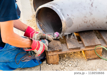 The worker prepares the edge of the weld joint for subsequent welding of the pipe 118058666
