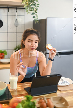 Young asian woman using digital tablet while having breakfast at home kitchen Young asian woman using digital tablet while having breakfast at home kitchen 118059237