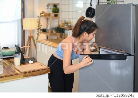 Young asian woman reaching for something inside the fridge, preparing for healthy meal Young asian woman reaching for something inside the fridge, preparing for healthy meal 118059243