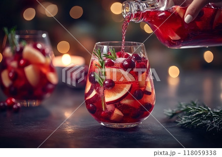 Female Hand Pouring Holiday Sangria in Glasses with Fruit Slice, Cranberry, and Rosemary on Dark Christmas Background 118059338