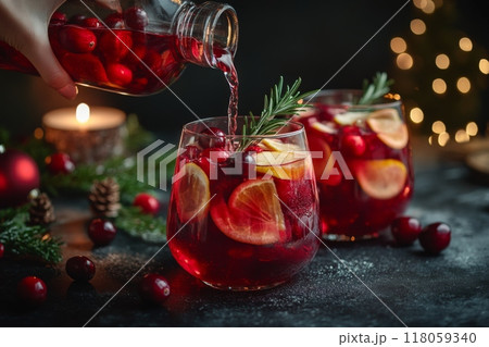 Female Hand Pouring Holiday Sangria in Glasses with Fruit Slice, Cranberry, and Rosemary on Dark Christmas Background 118059340