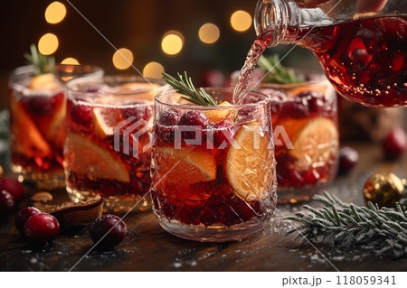 Female Hand Pouring Holiday Sangria in Glasses with Fruit Slice, Cranberry, and Rosemary on Dark Christmas Background 118059341
