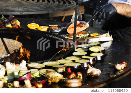 A person wearing black gloves is preparing food on a grill outdoors 118060420