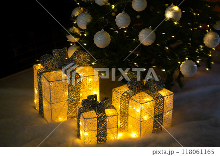 Decor of golden glowing boxes with bows under the Christmas tree. New Year's Eve banner. Decor of golden glowing boxes with bows under the Christmas tree. New Year's Eve banner. 118061165