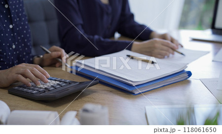Accountants or auditors reviewing financial documents while sitting at the wooden desk in office. Professionals analyzing paper reports and using calculators, side view. Audit and taxes Accountants or auditors reviewing financial documents while sitting at the wooden desk in office. Professionals analyzing paper reports and using calculators, side view. Audit and taxes 118061650