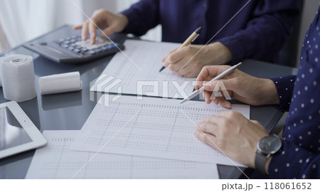 Two unrecognizable female accountants or auditors are sitting and reviewing financial documents in office. Audit and taxes Two unrecognizable female accountants or auditors are sitting and reviewing financial documents in office. Audit and taxes 118061652