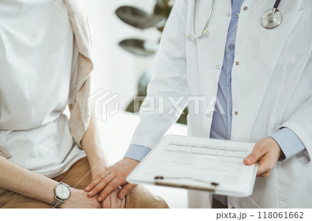 Doctor and patient in clinic. Friendly physician examining a young woman with a one hand while keeping a clipboard with medical records in another. Medicine concept Doctor and patient in clinic. Friendly physician examining a young woman with a one hand while keeping a clipboard with medical records in another. Medicine concept 118061662