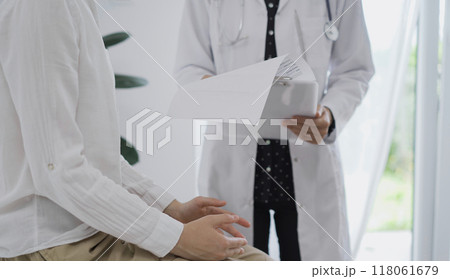 Doctor and a patient discussing something. The female physician, wearing a white medical coat standing with a clipboard during a consultation in the clinic, close up. Medicine concept Doctor and a patient discussing something. The female physician, wearing a white medical coat standing with a clipboard during a consultation in the clinic, close up. Medicine concept 118061679