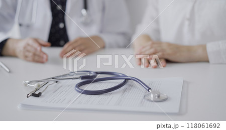 Stethoscope in focus while doctor and a patient gesturing with their hands during a consultation in the clinic. Medicine concept Stethoscope in focus while doctor and a patient gesturing with their hands during a consultation in the clinic. Medicine concept 118061692