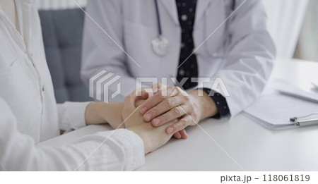 Doctor and a patient. The female physician, wearing a white medical coat over a dark blue dotted blouse, is reassuring a woman during a consultation in the clinic. Medicine concept 118061819