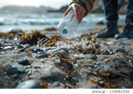 Person collecting plastic bottles on a pebble beach by the ocean shore 118062292