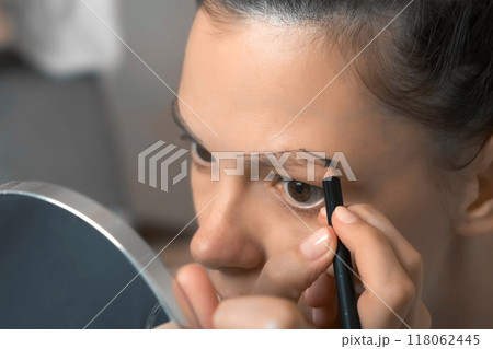 Young woman is painting contour of eyebrows using pencil before painting them. 118062445