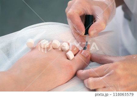 Pedicurist master is applying base coal for shellac on woman's nails on toes. Pedicurist master is applying base coal for shellac on woman's nails on toes. 118063579