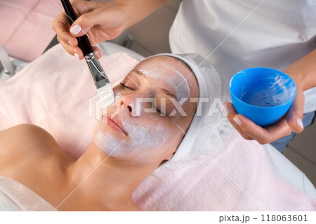Professional beautician is applying mask to woman's face using a brush. 118063601