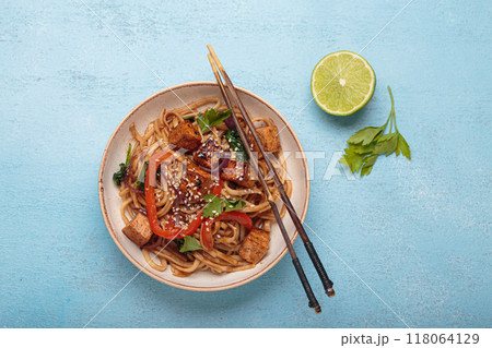 Bowl of vegetarian udon noodles with fried tofu and vegetables is served with chopsticks 118064129