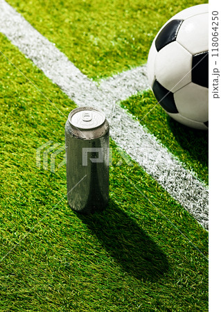 Soccer ball on green field, near white line. Chilled aluminum can of soda placed beside ball, casting shadow on grass. Soccer ball on green field, near white line. Chilled aluminum can of soda placed beside ball, casting shadow on grass. 118064250