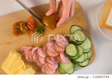 Woman cooking, hands cutting tomatoes on slices on wooden board. 118064794
