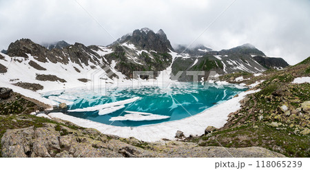 Lake in the mountain range, snow melting into the lake in summer. Foggy day in the mountains, panorama 118065239