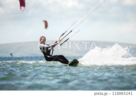 CLOSE UP, Fit Caucasian tourist kiteboarding along peninsula. Relaxed young woman surfing boarding and exploring Mediterranean coastline on sunny summer day 118065241