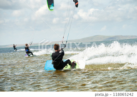 Kitesurfing, kiteboarding, action photo. Man from behind actively and quickly rides on water on kiteboard, sailing, adrenaline 118065242