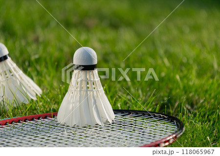 White badminton shuttlecock and badminton rackets on green grass in sunny shadow. Summer. Leisure games. Outdoors. Close up. 118065967