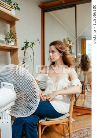fan cools unhappy Caucasian woman languishing in summer heat. warmed-up experiences hot flashes fan cools unhappy Caucasian woman languishing in summer heat. warmed-up experiences hot flashes 118066180