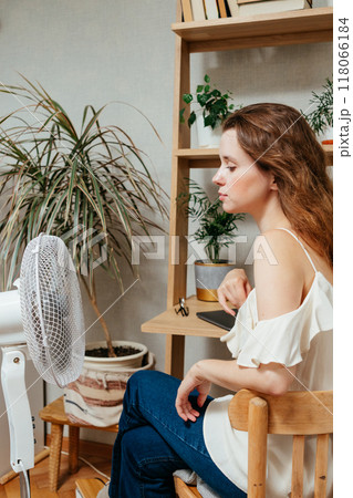 fan cools unhappy Caucasian woman languishing in summer heat. warmed-up experiences hot flashes 118066184