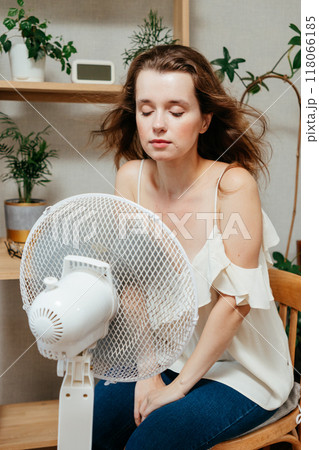 fan cools unhappy Caucasian woman languishing in summer heat. warmed-up experiences hot flashes 118066185