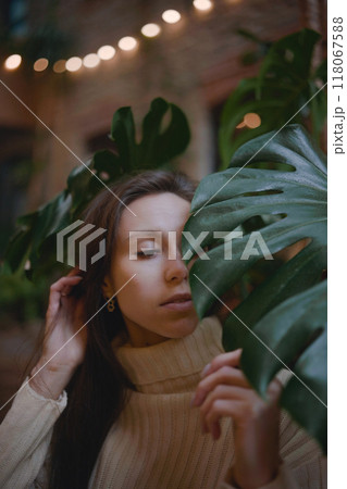Cozy indoor moment with a woman gently interacting with large green leaves during evening ambiance 118067588