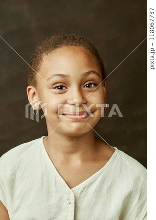 Vertical portrait of young smiling African American girl looking at camera posing on brown background at studio 118067737
