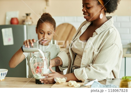 Cute African American girl making smoothie carefully adding milk to blender while 118067828