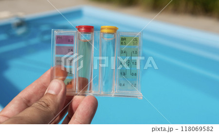 Hand holding a water testing kit over a clear blue pool, focusing on water quality and pool care. 118069582