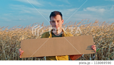 A man in a yellow shirt holds a blank cardboard sign while standing in a dry cornfield under a blue sky. A man in a yellow shirt holds a blank cardboard sign while standing in a dry cornfield under a blue sky. 118069590