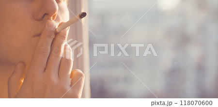 Young man is smoking cigarette near the window. Young man is smoking cigarette near the window. 118070600