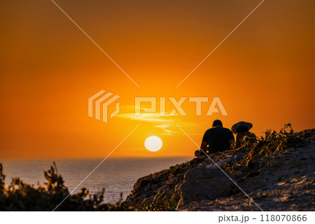 Young couple watching the sunset on the Barbate beach next to the Trafalgar lighthouse, Cadiz	 118070866