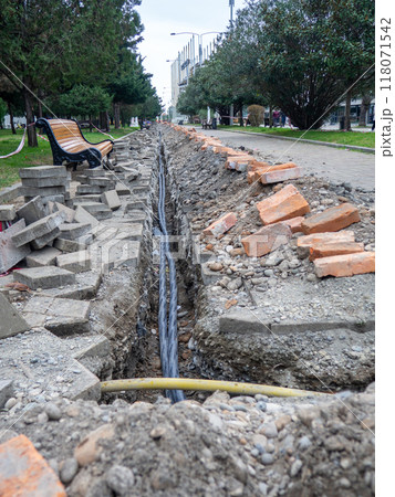 Broken sidewalk. Conducting the cable underground. Cable laying work. Communications in the city.  Digging a trench for wires. 118071542