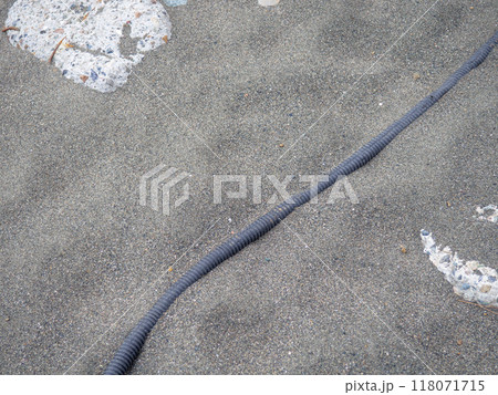Cable on black sand. The cable sticks out of the ground. Electrical communications on the beach. Industry. 118071715