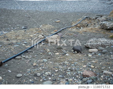 Cable on black sand. The cable sticks out of the ground. Electrical communications on the beach. Industry. 118071722