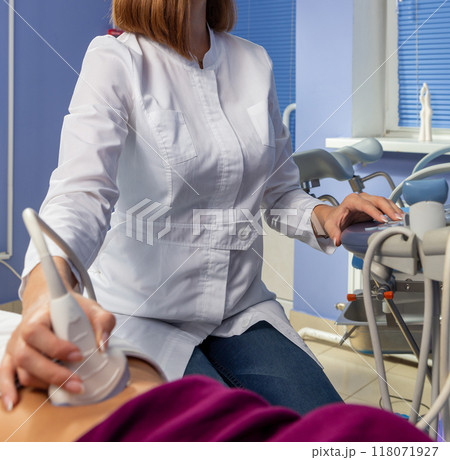 The doctor performs an ultrasound diagnosis of the abdominal cavity of a pregnant girl at an early stage of pregnancy. The doctor performs an ultrasound diagnosis of the abdominal cavity of a pregnant girl at an early stage of pregnancy. 118071927