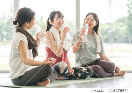 スポーツジムのヨガ教室で休憩をしながら水分補給・スポーツドリンクを飲む女性達 スポーツジムのヨガ教室で休憩をしながら水分補給・スポーツドリンクを飲む女性達 118076974