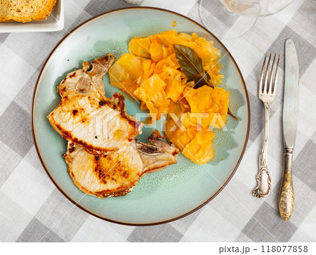 Plate contains two pieces of lean pork tenderloin on bone, garnished with stewed cabbage. 118077858