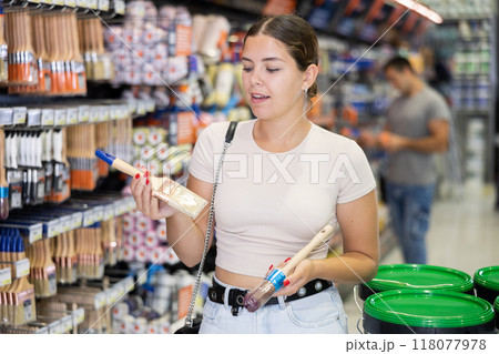 Smiling young woman choosing brushes in local hardware store Smiling young woman choosing brushes in local hardware store 118077978