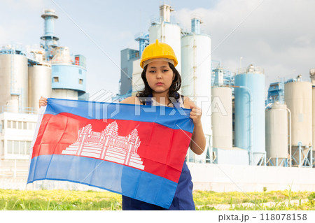 Worried asian girl in work clothes and hardhat with flag of cambodia standing in front of industrial scenery Worried asian girl in work clothes and hardhat with flag of cambodia standing in front of industrial scenery 118078158