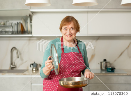 Adult woman in apron posing with frying pan Adult woman in apron posing with frying pan 118078360