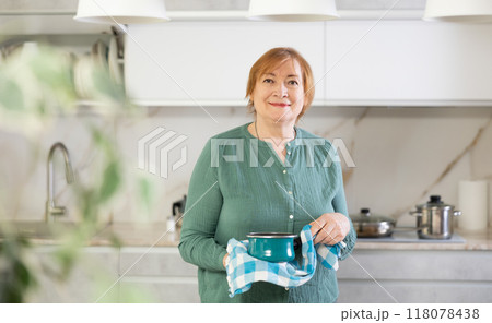 Happy older lady cooking in kitchen with warm smile 118078438
