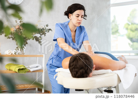 Female masseur doing massage at back man who lying on massage table in beauty salon 118078446