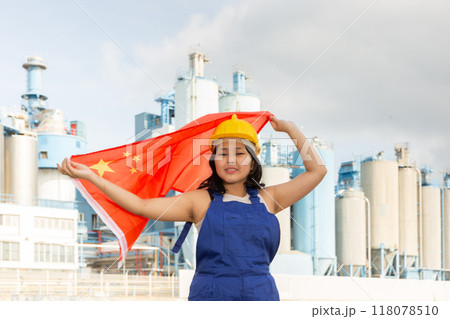 Teenage girl in blue overalls waving the flag of China against backdrop of modern metallurgical plant Teenage girl in blue overalls waving the flag of China against backdrop of modern metallurgical plant 118078510