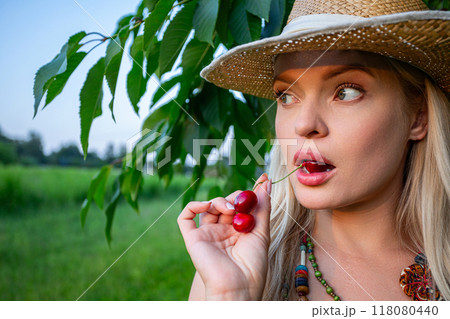 A woman holding a cherry in her mouth, looking sideways A woman holding a cherry in her mouth, looking sideways 118080440