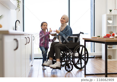 Muslim mother in wheelchair and daughter eating fresh salad together 118082909